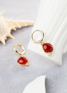 Close-up of gold-plated hoop earrings with red natural stone charms and zircon details