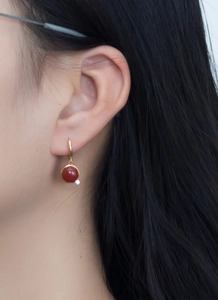 Detail of gold huggie hoop earrings with round red stone pendants and zircon accents