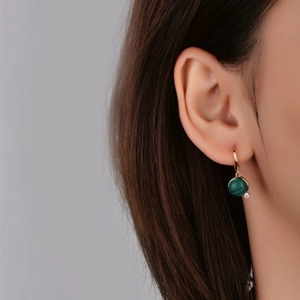 Golden drop earrings featuring circular malachite stone and zircon on a female model