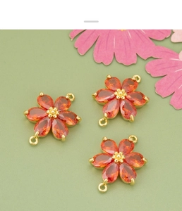 Makro-Detail von drei orangefarbenen Zirkon-Blütenanhängern mit vergoldeten Ösen für DIY-Schmuck