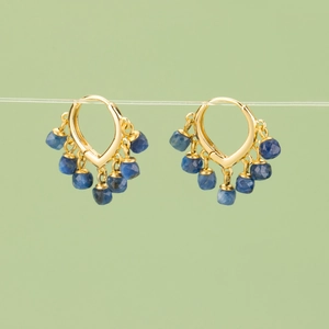 Elegant gold hoop earrings with hanging blue gemstone charms on a soft green background
