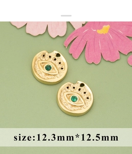 Macro detail of 12.3mm gold evil eye charms with green crystals and hammered texture