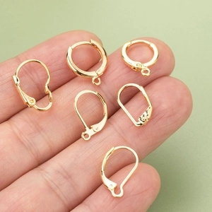 Golden leverback earring hooks and jewelry components displayed on fingertips