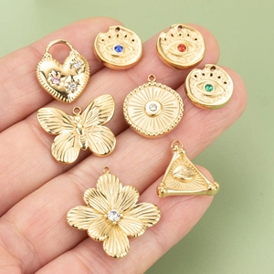 Eight gold-plated titanium steel charms including evil eye and flower pendants held by hand