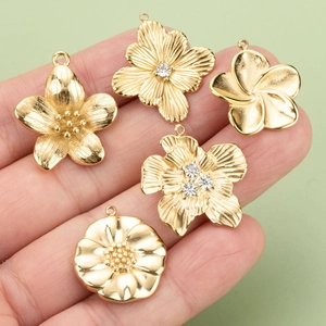 Vijf gouden bloemenhangers met strassteentjes in de hand als maatstaf voor DIY-sieraden maken
