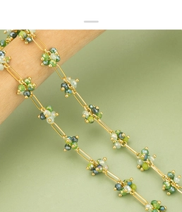 Macro detail of gold-plated paperclip chain with green beaded flower clusters