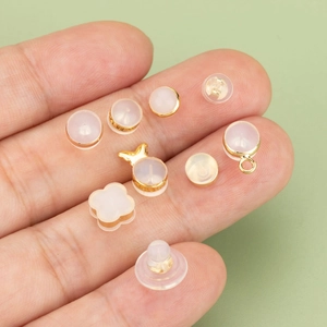 Assorted gold-plated earring backs and silicone plugs held in hand against green background