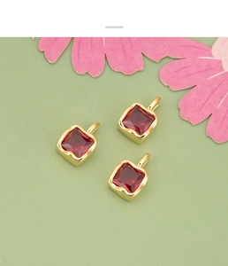 Close-up of three square red zircon pendants with gold plating on textured green background