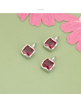 Detailed view of three square red zircon pendants with silver metal settings and top loops
