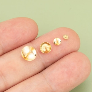 18K gold plated flat pad earring posts in four assorted sizes shown on a fingertip