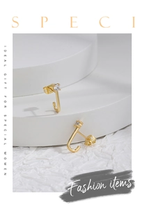 Macro view of gold J-shaped earrings with clear zircon stones on modern white displays