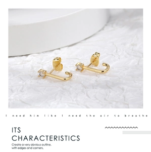 Detail of elegant J-shaped gold earrings with sparkling zircon on a textured background