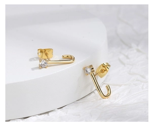 Close-up of J-shaped gold earrings with sparkling zircon inlay and butterfly backings
