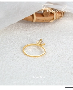 Detailed view of a gold six-prong solitaire ring with a round zircon on marble background