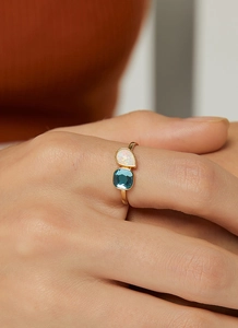 Primer plano detallado de un anillo dorado con ópalo en gota y gema azul profundo
