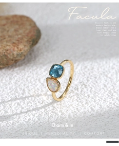 Detalle de un anillo dorado de doble piedra con cristal azul y opalo blanco de gota