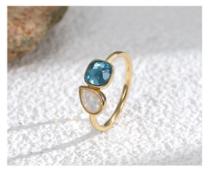 Detalle macro de anillo dorado con gema azul cuadrada y piedra de ópalo blanco de gota