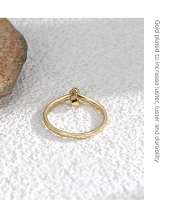 Detail of gold plated ring with cube pendant on natural stone and textured white surface