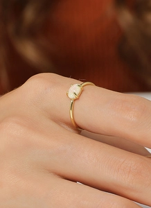 Nahaufnahme eines minimalistischen Goldrings mit weißem ovalem Opal in Vierklauenfassung