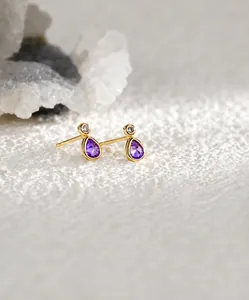 Détail macro de boucles d'oreilles dorées en forme de goutte avec zircon violet et cristal