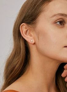 Close-up of geometric gold stud earring with white opal and pink triangle zircon