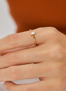 Detalle de anillo dorado con circón rectangular en modelo con fondo cálido suave