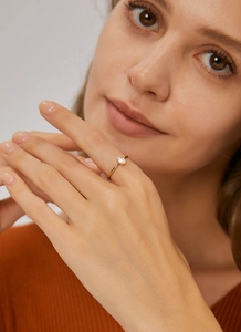 Elegante anillo fino dorado con circón rectangular lucido por una modelo con luz cálida