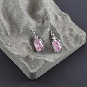 Detail view of silver earrings with rectangular pink zircon stones on grey stone background
