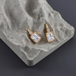 Detail of 18k gold plated rectangular zircon charms with sleek metallic frames and rings