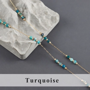 Close-up of turquoise beads on a gold stainless steel chain over a textured rock