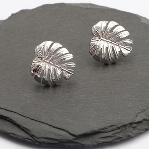 Polished silver monstera leaf stud earrings on textured stone base for jewelry DIY