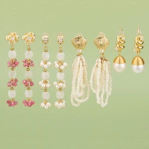 Ensemble de boucles d'oreilles dorées avec fleurs, perles et cristaux sur fond vert doux
