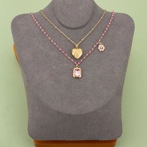 Gelaagde gouden ketting met hartjeshanger en roze kralen op een display voor sieraden