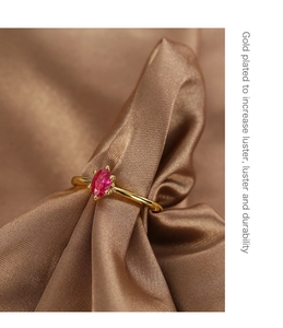 Macro view of gold plated ring with a vibrant red oval zircon on soft silk fabric