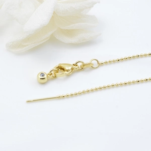 Verstelbare gouden kralenketting met karabijnsluiting en bedeltje op witte achtergrond