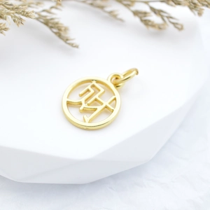 Golden round hollow charm pendant with ethnic symbols on a white display stand