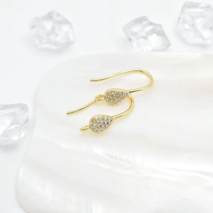 Elegante gouden druppeloorbellen met zirkonia op een witte schelp en kristallen achtergrond