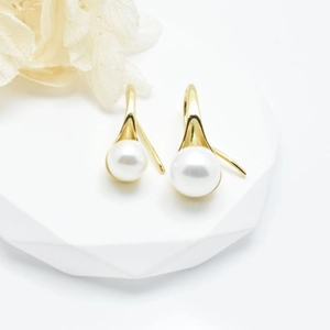 Elegant gold fishhook earrings with lustrous white pearls on a minimalist white platform