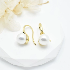 Elegant gold pearl drop earrings on white geometric stand with floral accents