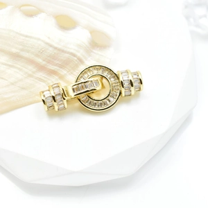 Golden round necklace clasp with baguette-cut zircons on a white geometric stand