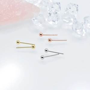 Boucles d'oreilles boules minimalistes en or, argent et or rose sur une surface blanche