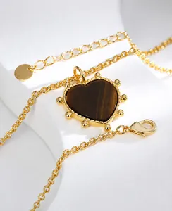 Close-up of heart-shaped tiger eye pendant on a gold necklace with beaded edge detail
