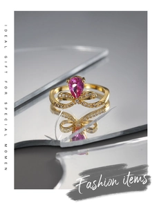 Detalle del anillo con circón rosa en forma de pera y lazo dorado sobre espejo roto