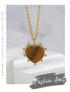 Macro detail of gold-tone heart pendant with tiger eye stone and beaded texture