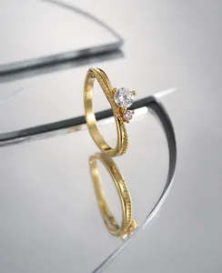 Detail of gold ring with round clear zircon and pink accent stone on a mirror surface