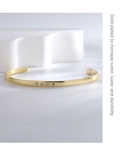 Macro view of gold plated open bangle featuring polished finish and four inlaid zircon stones