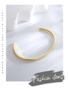 Detail of gold-plated open bangle with four inlaid zircons on a white textured background