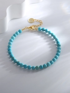 Detailed shot of blue turquoise beads bracelet with a gold clasp on a textured surface