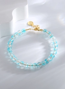 Détail d'un bracelet en perles de cristal bleu et clair avec fermoir doré et chaînette