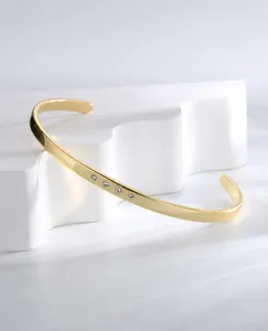 Detailed close-up of a gold-plated C-shaped cuff bracelet with four inlaid zircons